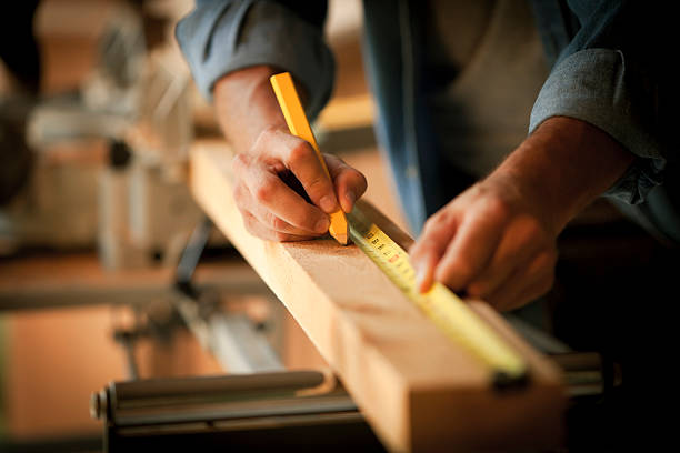 Closeup cropped view of a carpenter marking a measurement on a wooden plank. Horizontal shot.