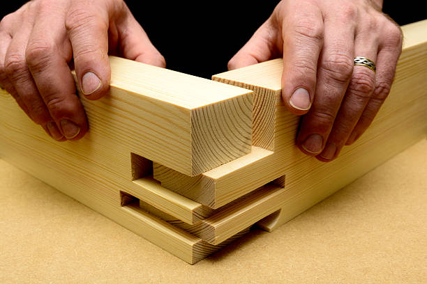 Shown as an exploded view, a craft person uses their hands to pre assembles a comb joint in soft wood, pine stock prior to gluing and sanding. This double mortice and tenon joint helps the carpenter achieve maximum glueing area and increased strength.